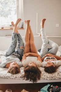 three women lying on bed while raising their feet